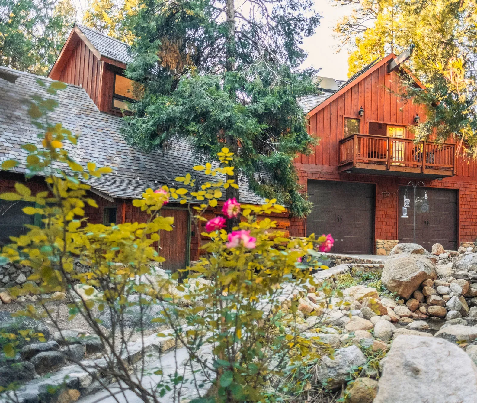 Root-Stone Lodge among cedars at golden hour, river-stone walls and wild roses in bloom